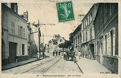 La rue de Paris dans les années 1900.Le tracé historique de la RN 14 est alors parcourue par le tramway Enghien - Trinité dont on voit les rails de la voie unique. C'est l'ancêtre du T8.