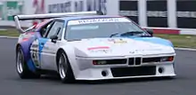 Une BMW M1 Procar blanche peinte dans sa diagonale aux couleurs de BMW Motorsport sur une piste de course