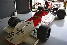 Photographie d'une monoplace de Formule 1 rouge et blanche, vue de trois-quarts dans un stand d'exposition.
