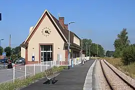 Vue générale de la gare en direction de Trouville - Deauville avec une vue sur la façade latérale du bâtiment voyageurs où se trouve l'accès à l'espace d'attente.