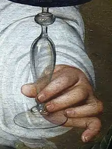 Détail de la peinture : une main tient un verre en cristal rempli de vin rouge.