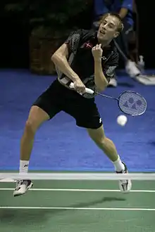 Joueur de face, en suspension, tenant une raquette de badminton.