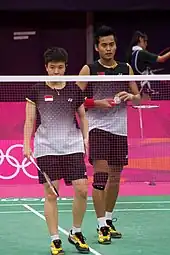 Deux joueurs de badminton se tiennent debout derrière le filet.