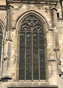 Dans un mur de pierres, encadrée par deux niches, une grande fenêtre composé de quatre lancettes, surmontées par des formes géométriques