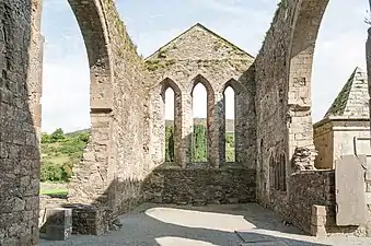 Photographie représentant le chevet intact d'une église ruinée, à trois fenêtres ogivales.