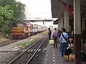 Quai de gare bordé par des voies de chemin de fer dont l'une est empruntée par un train.