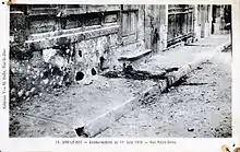 Carte postale ancienne en noir et blanc du trottoir d'une rue et d'une façade abîmée par une explosion.