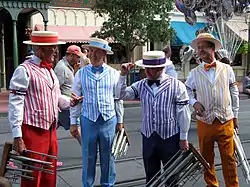 Quatre membres d'un barbershop portant chacun une tenue d'une couleur différente. Ils sont habillés en chemise avec nœud papillon, pantalon et chapeau.