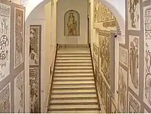 Perspective dans le département des mosaïques romaines vu de l'escalier d'accès avec des mosaïques au mur et une statue d'Apollon au fond.