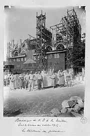 Photographie en noir et blanc d'ouvriers et de blocs de pierre devant les échafaudages du chantier.