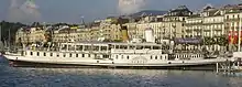 Photographie en couleurs d'un bateau à vapeur blanc devant des immeubles.