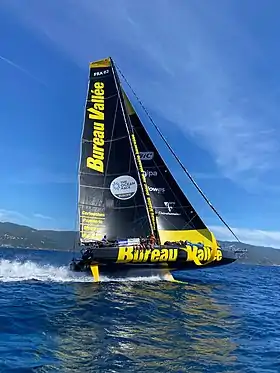 Bateau noir et jaune, sous voile, vu en entier, de côté, en mer.