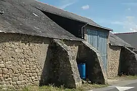 Photographie d’un bâtiment en pierre, aux contreforts saillants, et à la porte bleue.