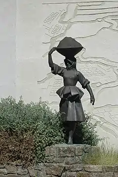 Photographie d’une statue en bronze représentant une femme en costume traditionnel portant une charge sur la tête.