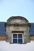 Photographie d'une lucarne arrondie, sur fond de toit en ardoise.