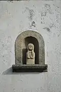 Photographie d'une niche de façade en granit, contenant une statuette.