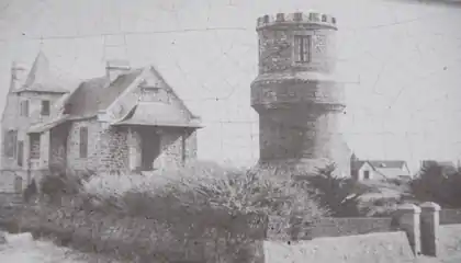 Vue en noir et blanc d'une tour crenelée s'élevant devant un manoir breton.