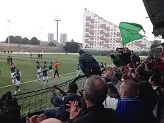 Photographie d'un stade de football avec des supporters en premier plan et des joueurs à l'arrière-plan.