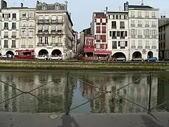 Vue de bâtiments se reflétant dans un cours d’eau.
