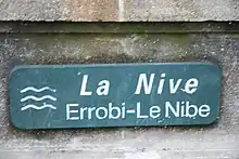 Photographie d'un panneau trilingue indiquant un cours d’eau.