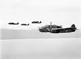 Quatre avions militaires bimoteurs en vol à basse altitude au-dessus de l'océan.