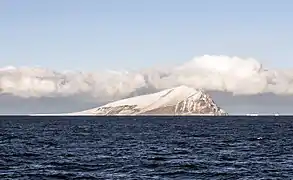 Île montagneuse enneigée avec deux icebergs au loin.