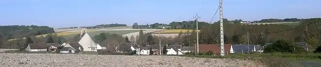 Photographie en couleur d'un alignement de maisons dont émerge le pignon d'une église moderne.