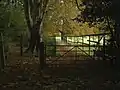 Chemin fermé par une barrière en bois sous des arbres.