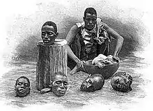 Gravure présentant un homme assis devant quatre têtes humaines coupées, sur le sol, et une cinquième sur un billot de bois dressé.