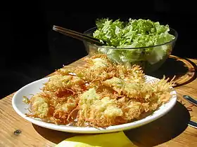 Tas de beignets chevelus croustillants sur une assiette blanche, devant un plat de salade croquante.