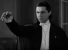 Photographie en noir et blanc de l'acteur Béla Lugosi costumé en comte Dracula, avec une cape noire, une chemise blanche et un nœud papillon.