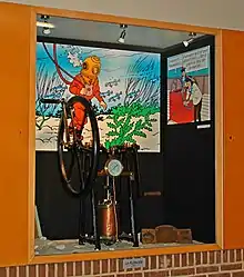 Des images agrandies extraites de l'album servent de décor à une pompe exposée dans une vitrine.