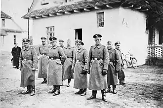 Groupe de soldats portant de longs manteaux devant une maison blanche