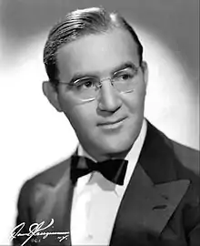 Benny Goodman, photographié en 1942, porte des lunettes, il est habillé d'un smoking et d'un nœud papillon. Ses cheveux sont gominés, avec une raie sur le côté gauche de son visage. La photo est en noir et blanc, l'éclairage est assez doux. La mise au point est faite sur son visage.