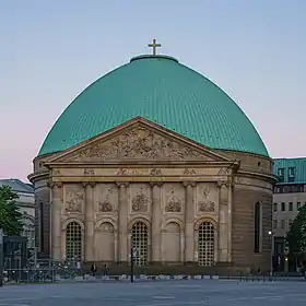 une façade rosâtre à cinq travées entourées de colonnades surmontées d'un fronton de facture néo-palladienne cache un immense dôme bleu-vert surmonté d'une croix dorée.