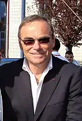 Photographie d'un homme vêtu d'une chemise blanche, d'une veste noire et porteur de lunettes de soleil
