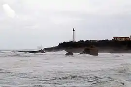 Vue d'une pointe rocheuse couronnée par un phare et s'avançant sur la mer.