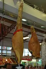 Photographie de deux jambons pendus, dans un marché.