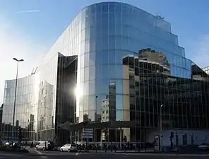Photographie de la bibliothèque Mériadeck. Un haut bâtiment moderne entièrement en verre reflétant le soleil.