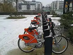 Vélos orange alignés, petite couche de neige blanche qui recouvre le sol.