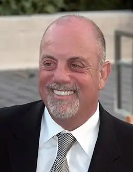 An upper body shot of a man wearing a shirt, suit and tie. He is balding and his smiling mouth is framed by a white goatee beard.