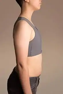 Vue de profil d'une jeune personne imberbe ayant la poitrine compressée par un bandage spécifique de type soutien-gorge