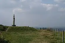 un monument en forme d'obélisque se dresse sur un terre-plein herbeux au sommet d'une colline.