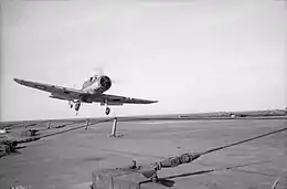 Photo en noir et blanc d'un avion à hélice appontant sur un porte-avions.