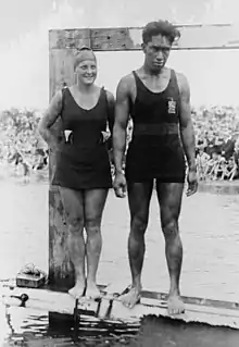 Photographie montrant Ethelda Bleibtrey et Duke Kahanamoku en costumes de bains, debout et côte à côte au bord de l'eau.