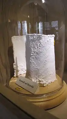 Photographie en couleur d'un bloc de produit blanc placé sous une cloche en verre dans une salle d'exposition.