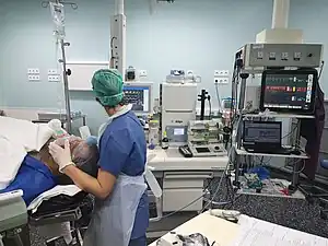 Infirmière anesthésiste au bloc opératoire, placée à la tête du patient à endormir et surveillant les constantes sur des écrans