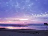 Plage lors du coucher du soleil. La couleur du ciel est violette et les nuages sont roses.