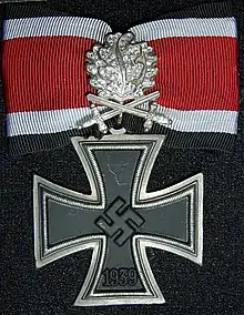 Distinction militaire métallique ayant la forme d'une croix pattée germanique avec un ruban rouge.