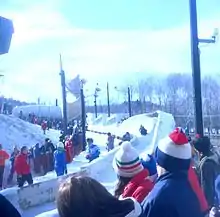 La piste de bobsleigh avec du public de chaque côté et un bob qui arrive.